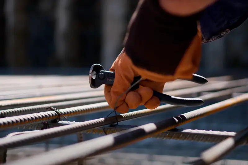 Gloved hand tying rebar with wire cutters on a construction site